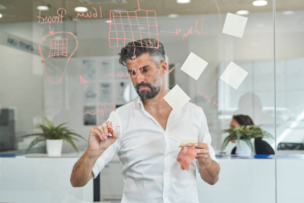 istock Serious ethnic man drawing scheme on glass board 2150860377