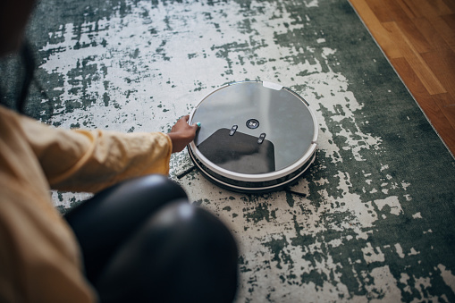 A person's hand interacts with an advanced robotic vacuum cleaner on a rug, illustrating the ease of technology