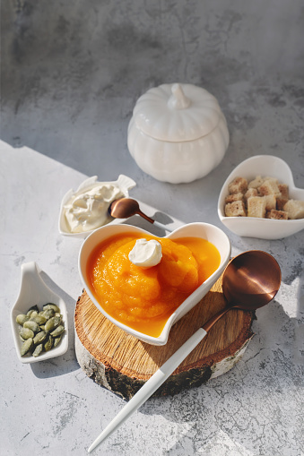 Pumpkin puree soup with yogurt, sesame seeds and pumpkin seeds in a heart-shaped bowl. All-season vegan diet soup.