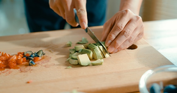 Closeup of young Asian man slicing avocado on cutting board at modern home. Diet and healthy food morning routine concept.