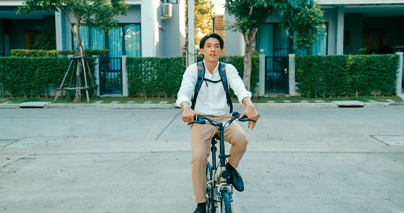 Young Asian businessman enjoys an environmentally friendly commute, cycling through the city at sunset with relaxed, sustainable lifestyle. Eco-Friendly commuting with bicycle concept.