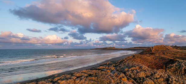 Aerial panorama landscape view of sand dunes and sandy beach at Embleton Bay and Dunstanburgh Castle on the England Coast Path at sunset