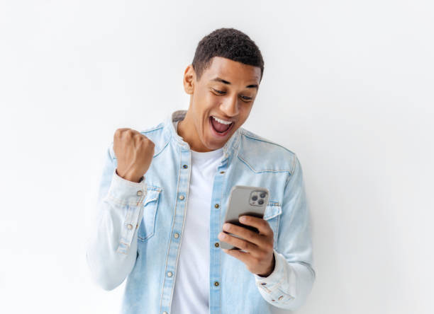 Excited young man holding mobile phone standing on white background