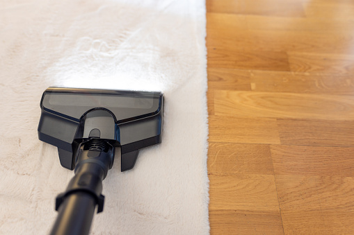 Above view of an unrecognizable person cleaning white carpet with stick vacuum