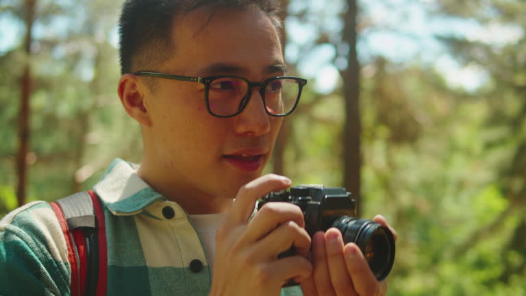 Asian man taking photo in forest, tourist photographer using camera , safe travel and explore, walking hiking tours. Traveling and hiking alone. Summer tourism, wild nature.