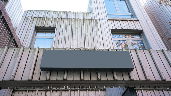 Blank black signboard mounted on weathered wooden facade of building perfectly suited for branding or advertisements. Structure urban style complements its simplistic yet impactful visual appeal.