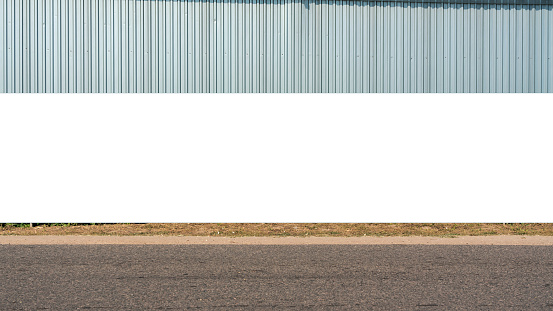 Large blank billboard on road with corrugated metal wall in background ready for graphic display or advertising. Perfect for high visibility in urban setting.