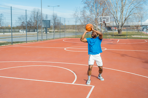 With playful prowess, a young African American man lights up the basketball court, his joyful approach to the game making it enjoyable for players and spectators alike