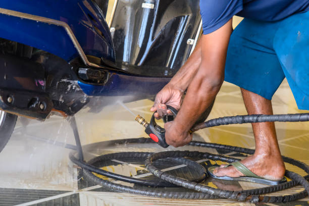 Worker cleaning motorcycle with high pressure water jet at service station