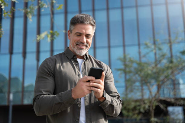 istock Confident mature hispanic senior business man using smartphone cellphone app standing at office building. Latin middle age male entrepreneur businessman holding mobile cell phone, working remotely 2150877755