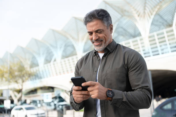 istock Confident mature hispanic senior business man using smartphone cellphone app standing at office building. Latin middle age male entrepreneur businessman holding mobile cell phone, working remotely 2150877769