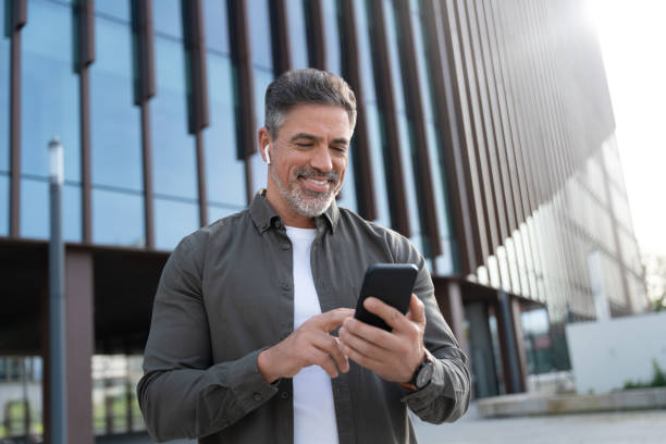 40s mature confident busy businessman entrepreneur using cellphone mobile phone for talking with family, business partners. Successful mid age man investor communicating on smartphone standing outdoor