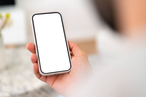 Man holding a mobile phone with a blank white screen Man holding a mobile phone with a blank white screen. Home interior can be seen in the background. Close up. man looking at phone over shoulder stock pictures, royalty-free photos & images