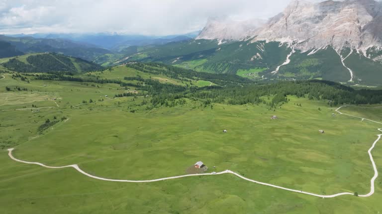 Aerial tilt down view of the lush green meadows of Pralongia in the Italian Dolomites. Drone is flying up fast revealing old cottages and winding unpaved roads and paths. LuPa Creative.