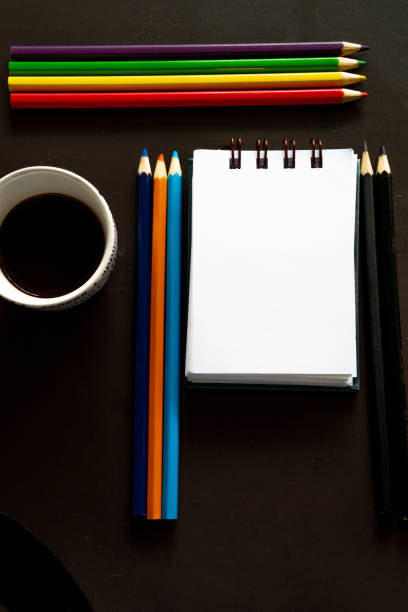 A Notepad on A Desk, Next To Some Colored Pencils and a Cup off Coffee.