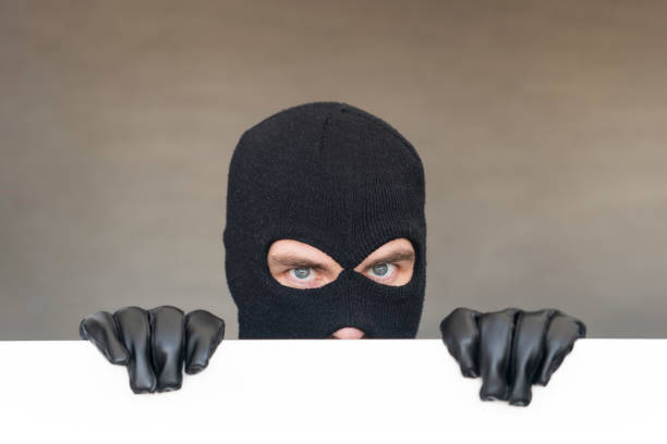 An evil thief in a mask looks out from behind a white board. Space for text and design. copy space.