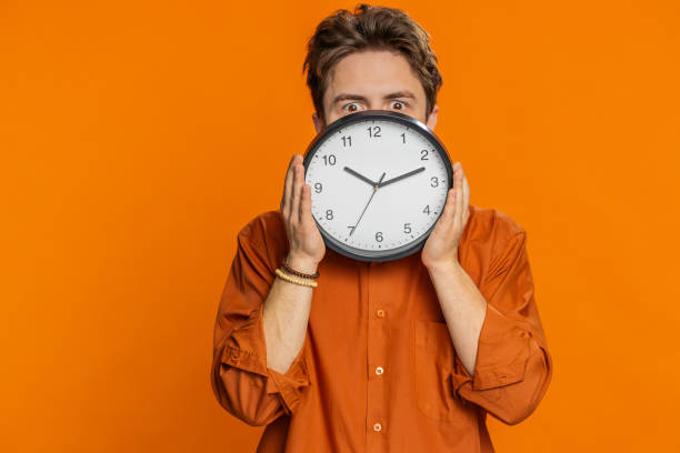 istock Serious strict young man holding office clock hiding behind checking time on watch obscuring face 2150890201