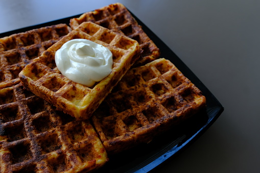 Belgian waffles on a black plate, on the biege table and souse it in sour cream