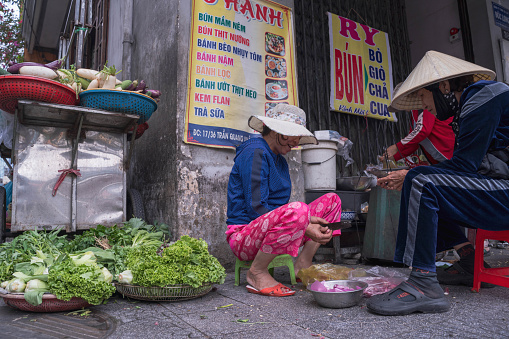 Hoi An City, Vietnam - February 28, 2024: A simple street stall in Hoi An, Vietnam, where women are selling and sorting vegetables.