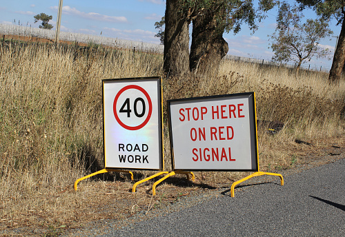 Two road work signs placed side by side on a grassy roadside in Australia