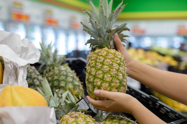 istock Female hands picking up a pineapple from a supermarket shelf. 2150903566
