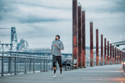 An athletic Filipino man takes a run across a bridge overlooking the Willamette River in Portland, Oregon while exercising outside.