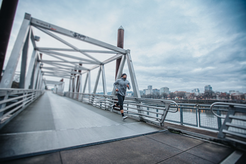 An athletic and healthy man of Filipino descent jogs across a city pedestrian footbridge on a beautiful, chilly Winter day in Portland, Oregon.