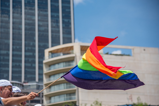 Mexico City, parade LGBT community Mxico City. 08/07/2019 A man holds a rainbow flag in front of a tall building. The flag is waving in the wind, and the man is wearing a hat. Concept of pride and celebration