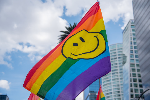 Mexico City, parade LGBT community México City. 08/07/2019 A rainbow flag with a smiley face on it. The flag is being held up in the air LGTB