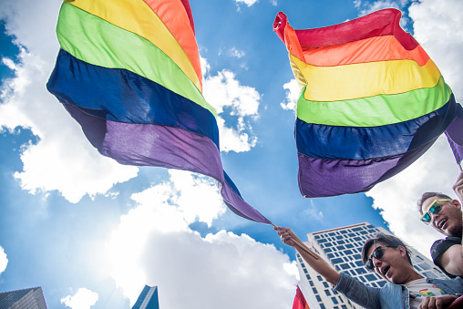 Mexico City, parade LGBT community México City. 08/07/2019 A rainbow flag is being held by two people in a city. The flag is flying high in the sky, and the people are smiling. Scene is joyful and celebratory, as the people are participating in a pride parade