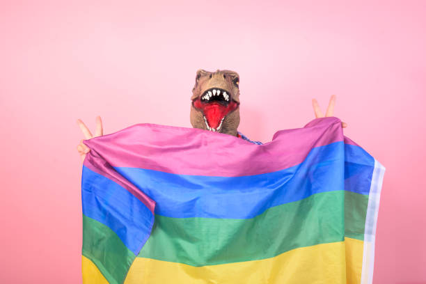 istock non-binary person with dinosaur head waving a rainbow flag on an isolated pink background 2150913075