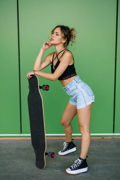 istock Beautiful young woman with longboard posing on green background 2150915113