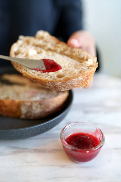 A woman spreading strawberry jam on sourdough bread