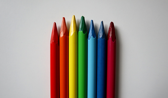 Photo of colored pencils arranged in the colors of the rainbow on white background. Pencils without wood. Pencils are placed in the middle from the bottom of the background. Different sizes.