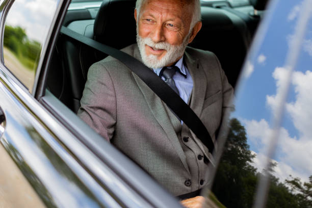 istock Senior gentleman in a sharp suit smiling while buckled up in his car 2150919090