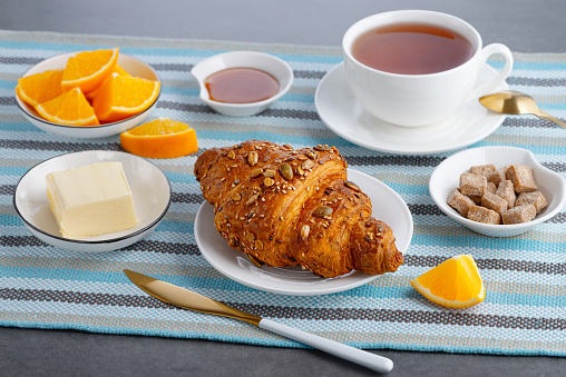 Fresh croissant with butter and tea, orange for breakfast.