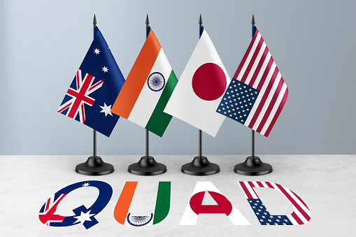 The national flags of Australia, India, Japan, and the United States displayed on desk stands with the acronym 'QUAD' prominently featured in front.