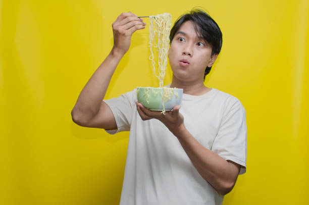istock Asian Man eats noodles in a bowl by lifting them with a fork snd chopstick. 2150926294