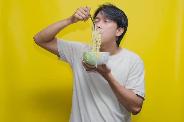istock Asian Man eats noodles in a bowl by lifting them with a fork snd chopstick. 2150926371