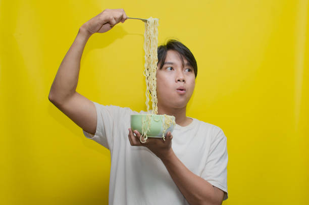 istock Asian Man eats noodles in a bowl by lifting them with a fork snd chopstick. 2150926469