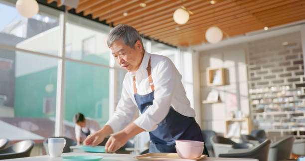 istock senior male waiter clean table 2150926766