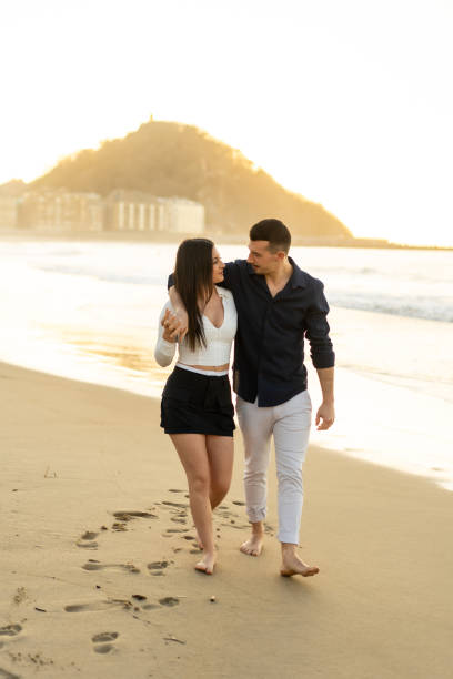 istock Young chic couple walking barefoot along the beach during sunset 2150927719