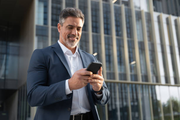 successful mature hispanic senior business man using smartphone cellphone financial application. indian or latin confident middle age male entrepreneur businessman holding mobile cell phone for invest - använda telefon bildbanksfoton och bilder