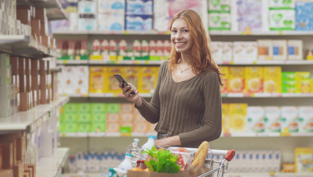 istock Smiling woman doing grocery shopping and using her smartphone 2150927971