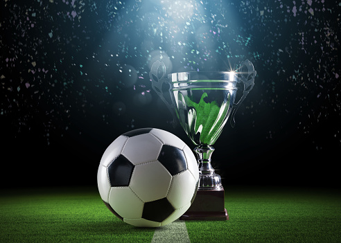 Shiny champions cup and football ball on the stadium field, sports and celebration concept, copy space