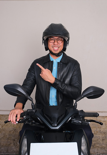A man sitting on the motorcycle smiling at the camera and pointing beside him