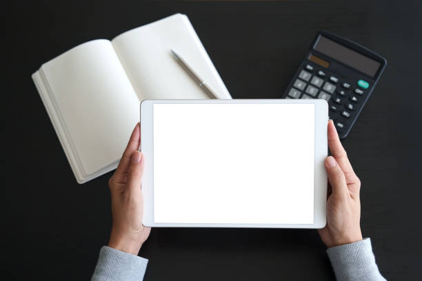 Over the shoulder view of an Asian woman using a digital tablet with a blank screen on working desk, illustrating the blend of lifestyle and technology.
