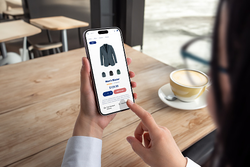 Woman shops for men's blazer on smartphone. Modern ecommerce app interface concept for effortless browsing and purchasing of stylish clothing