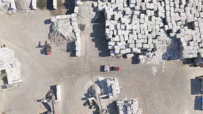 Top down drone shot of forklifts moving garbage cubes, sunny day at a scrapyard