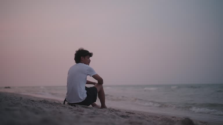 Rear view of a man sitting alone by the sea in the evening